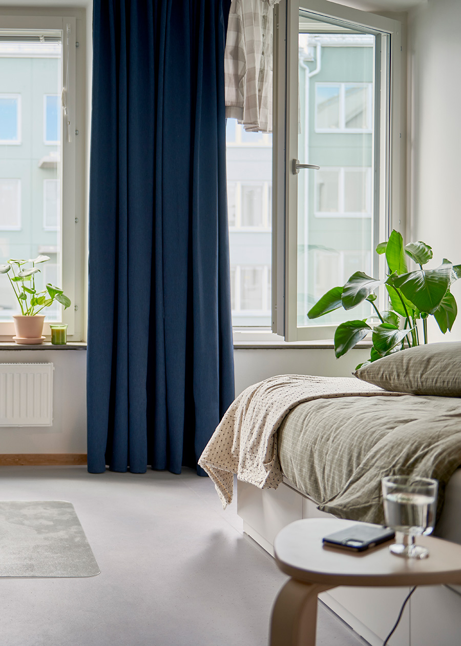 Un dormitorio en tonos beige con una cortina ANNAKAJSA azul hasta el piso cubriendo la mitan de una ventana.