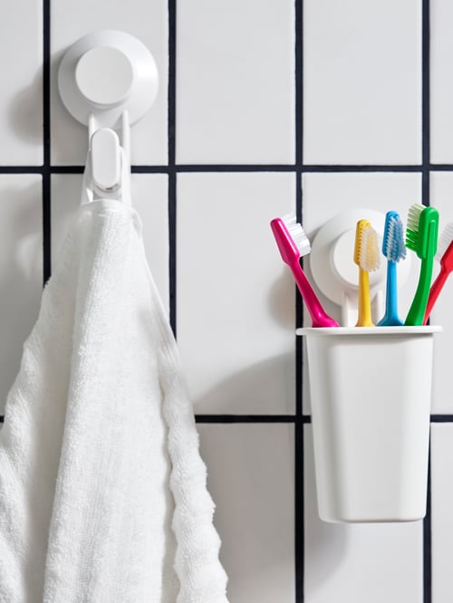 Bathroom wall with white towel hanging off a hook with suction cup and some toothbrushes in a toothbrush holder.