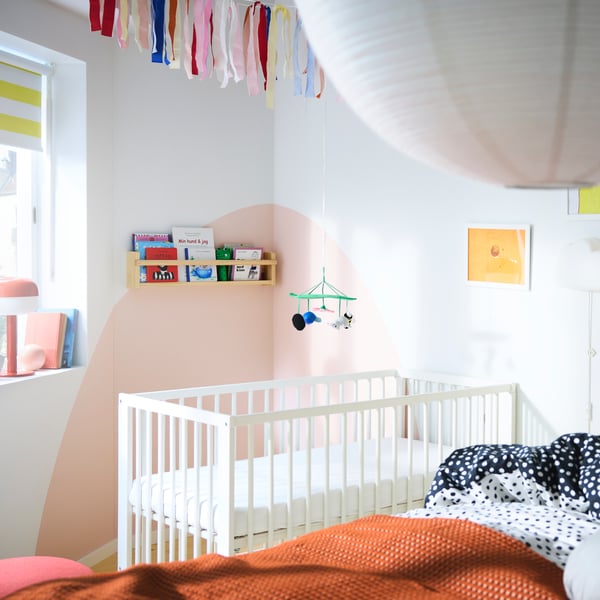 Bedroom with a big bed in the foreground and a baby cot in the background, different shelves with books and many paintings.