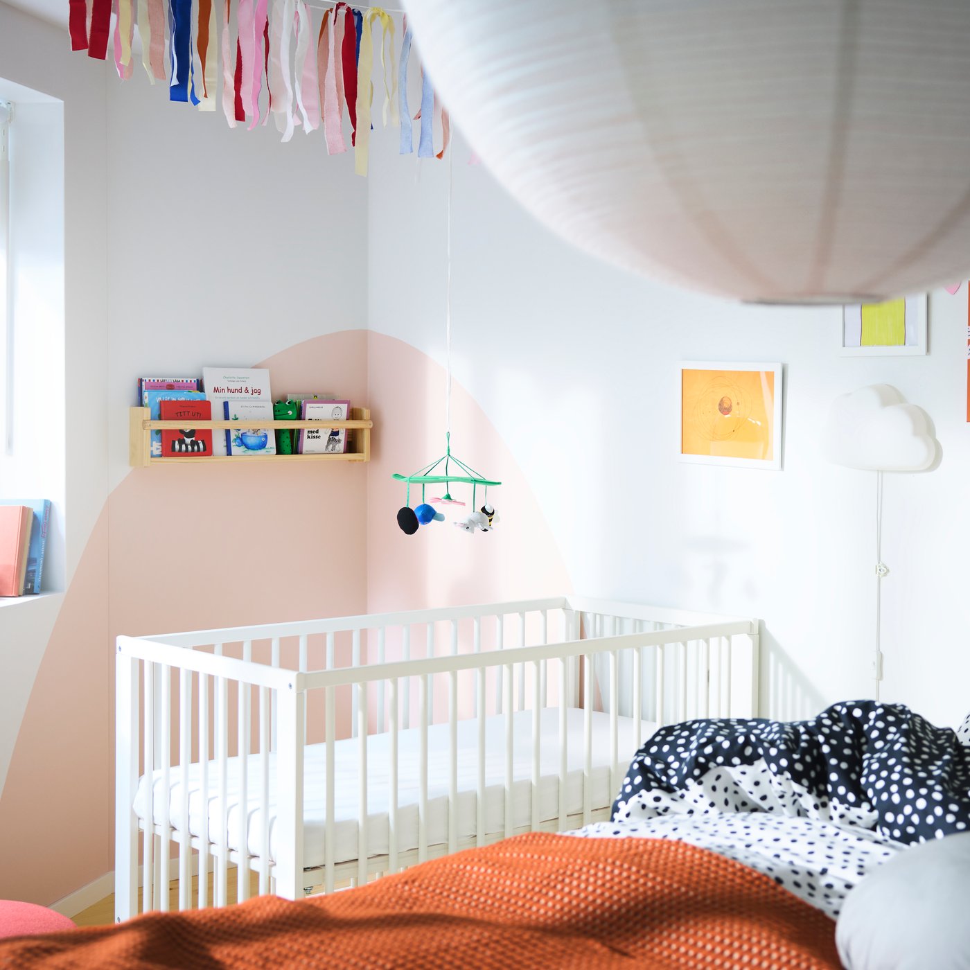 Bedroom with a big bed in the foreground and a baby cot in the background, different shelves with books and many paintings.