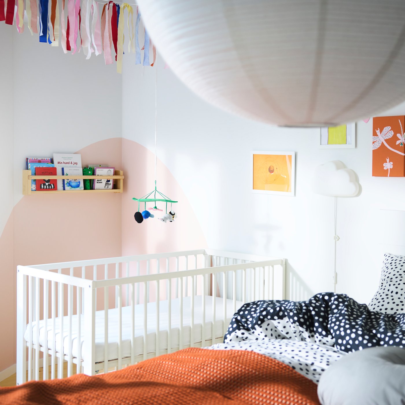 Bedroom with a big bed in the foreground and a baby cot in the background, different shelves with books and many paintings.