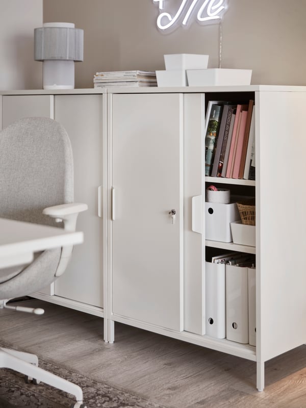 Two white TROTTEN cabinets with sliding doors, a partly open door revealing paperwork in white KUGGIS magazine files.