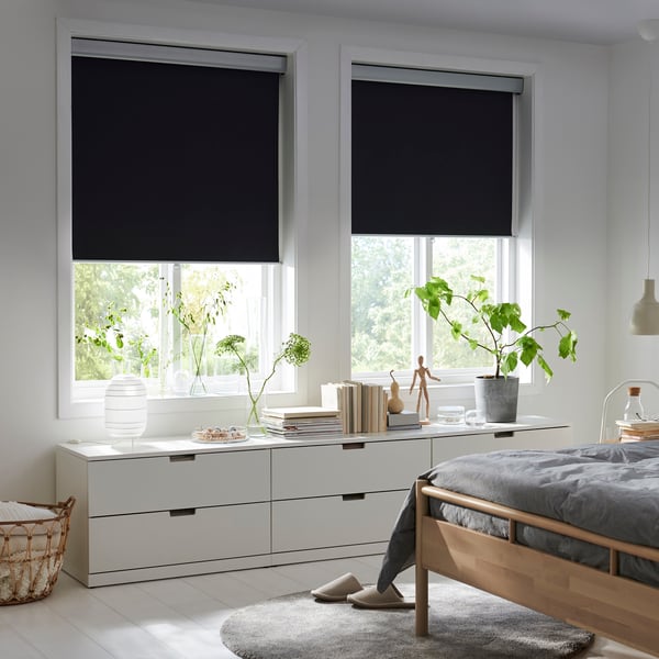 Una camera da letto con due finestre con tende nere abbassate a metà.