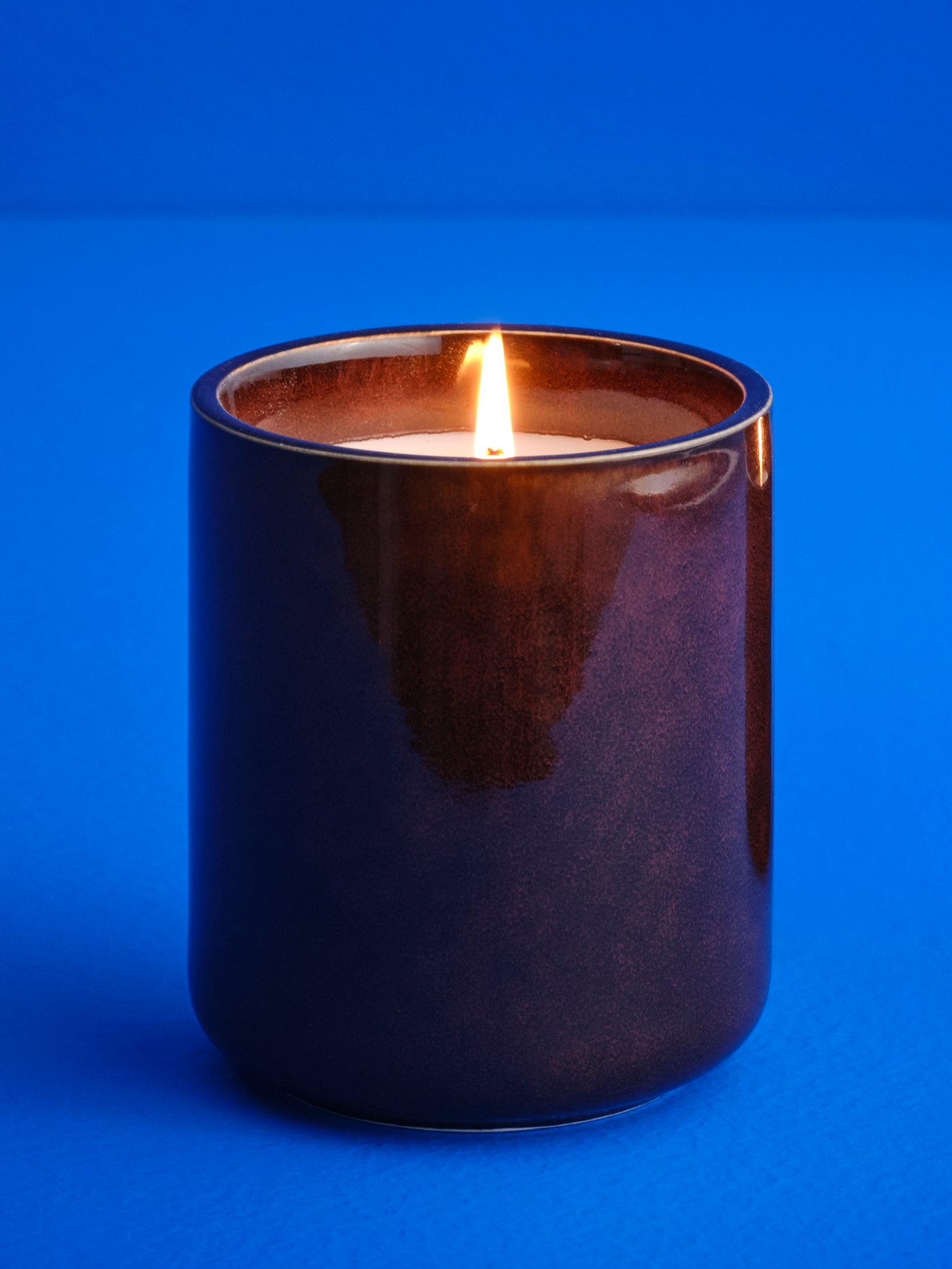 A lit KOPPARLÖNN almond and cherry scented candle, in a bright blue space.