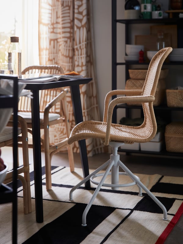 A beige-and-white STIGBYGEL swivel chair placed by a dining area with SALNÖ rattan seating around a black LISABO table.