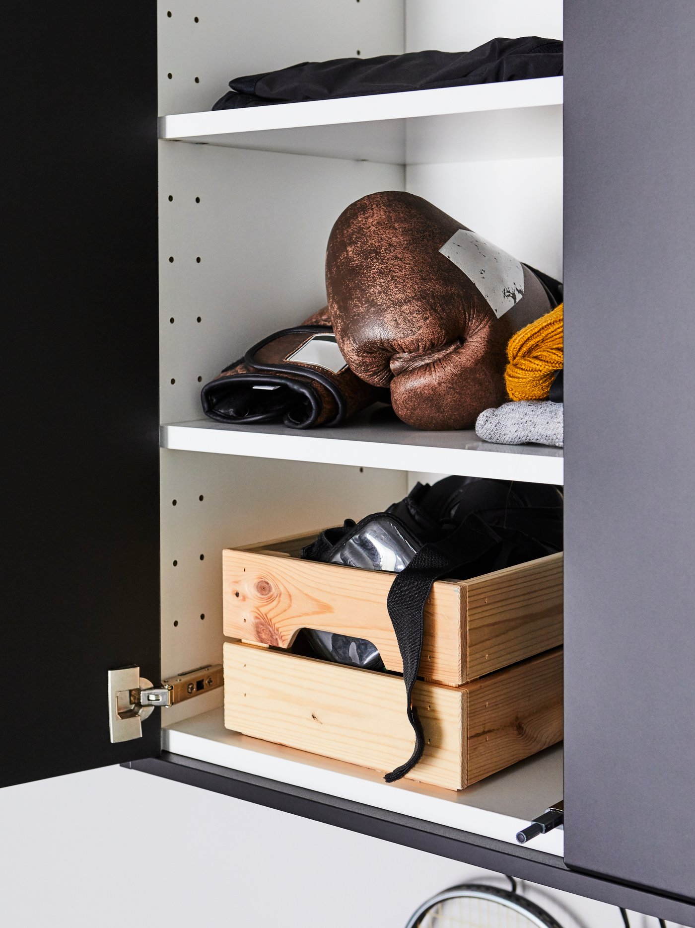 Un clóset abierto con guantes de boxeo en el compartimiento central y una caja KNAGGLIG con material deportivo en el compartimiento inferior.