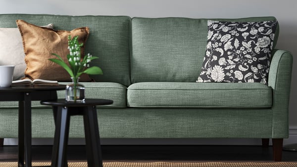 Grön EKHOLMA soffa med mönstrade kuddar och sidobord i en varm vardagsrumsmiljö.