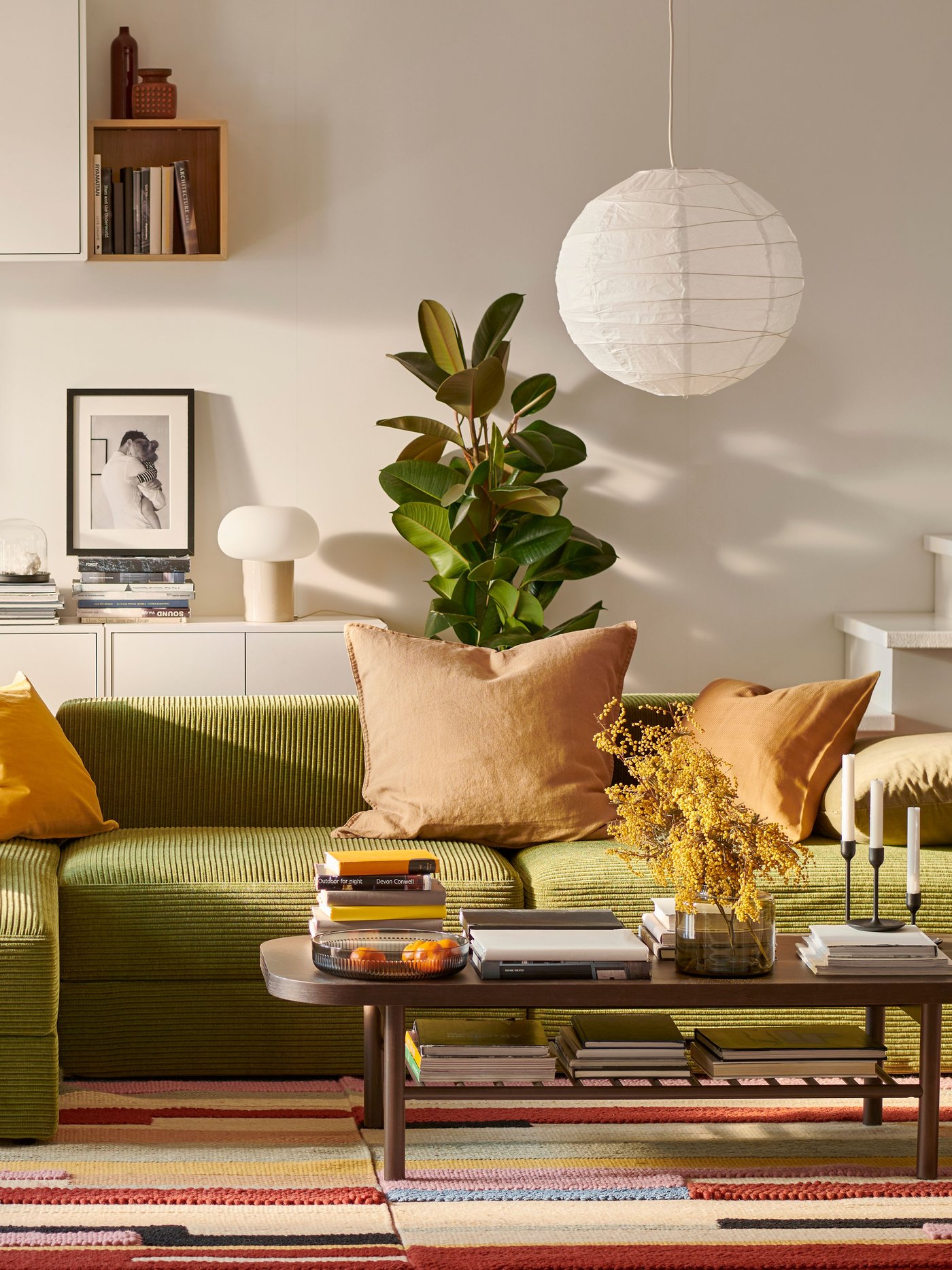 Ein JÄTTEBO-Sofa mit Chaiselongue und ein LISTERBY-Couchtisch stehen in einem Wohnzimmer auf einem bunten BRÖNDEN-Teppich.