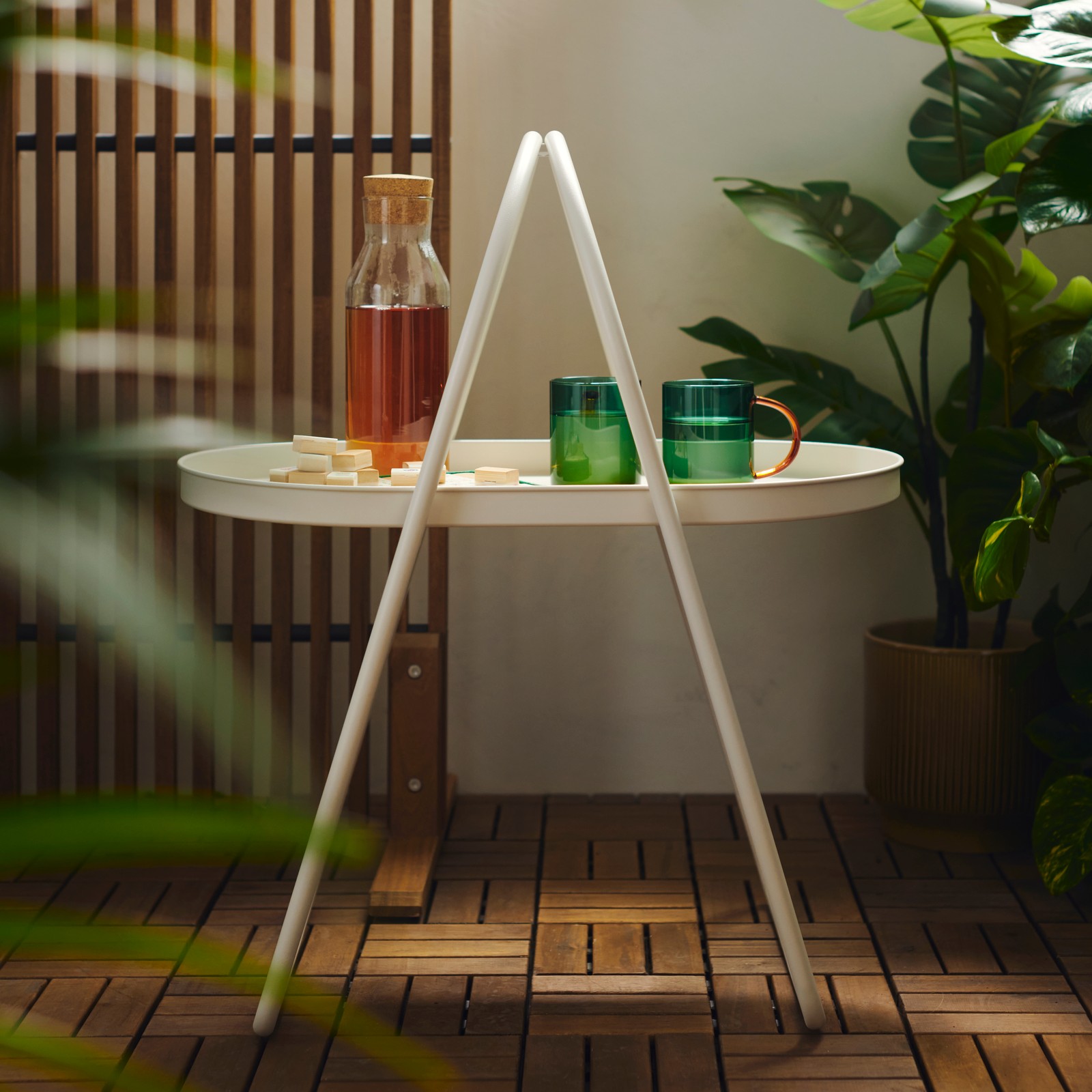 A balcony features a white MÅBÄRSSKÄR coffee table with a convenient handle, surrounded by green plants and wooden floor.
