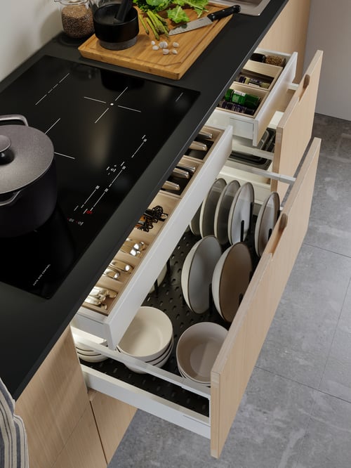 Une cuisine moderne dans laquelle se trouvent un panneau perforé pour tiroir, une table de cuisson à induction, un range-couverts, un range-couteaux et un porte-épices. 