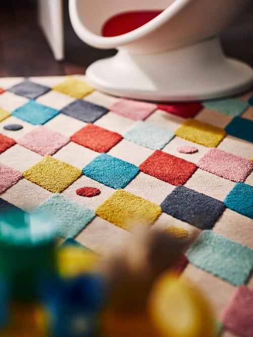 Close-up on children’s room floor with fun rectangular rug made of recycled plastic, with multicolour harlequin pattern.