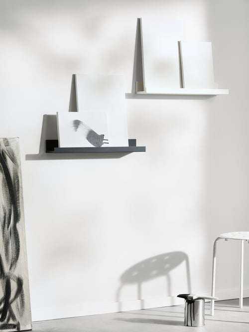 Living room featuring a black picture ledge made of fibreboard, placed on a white wall, next to a white picture ledge.