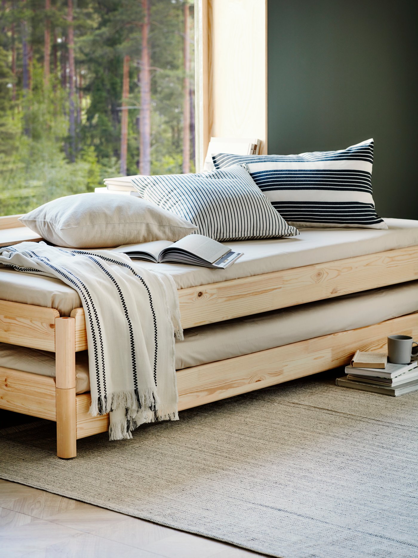 Una cama apilable con dos colchones con varias almohadas, una colcha y un libro abierto encima, y libros en el suelo.