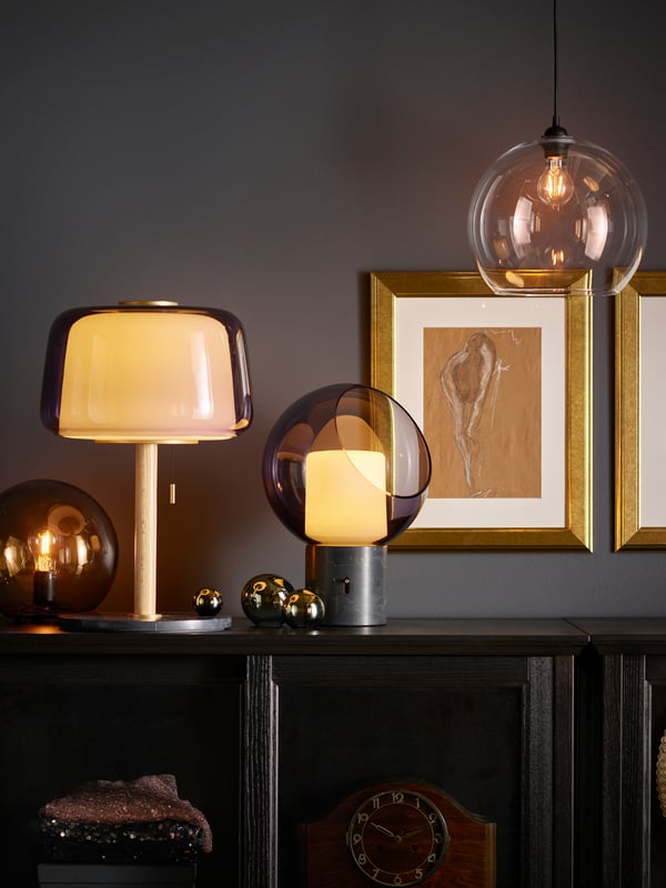 EVEDAL table lamp on top of a BESTA storage cabinet cupboard next to a FADO lamp. next to a few picture frames which are mounted on the wall. 