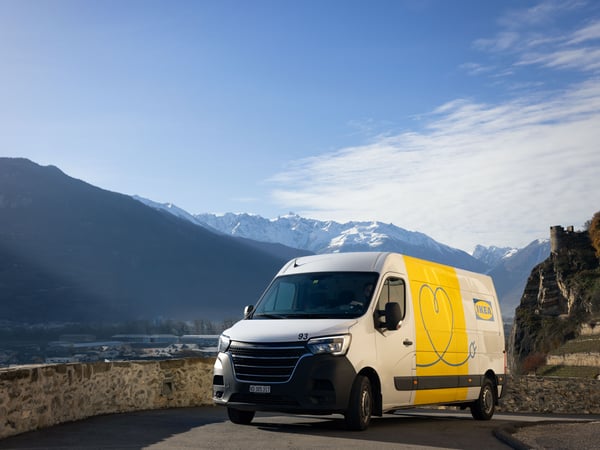 Un veicolo elettrico per le consegne IKEA su una strada in Svizzera, con il cielo azzurro e una catena montuosa parzialmente innevata sullo sfondo.