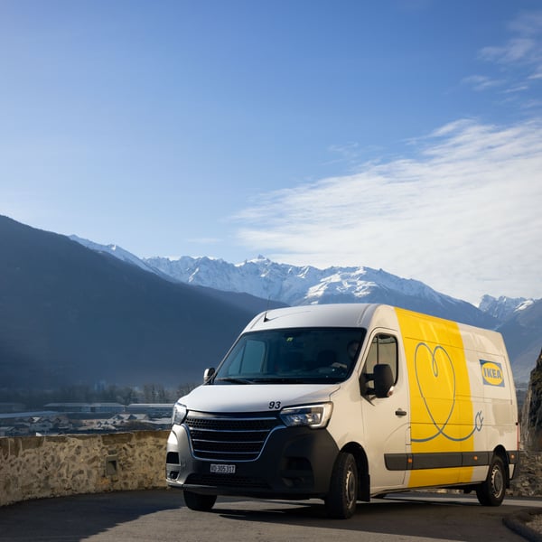 An IKEA delivery EV on a road in Switzerland, the sky is blue and there's a partially snow covered mountain chain in the background.