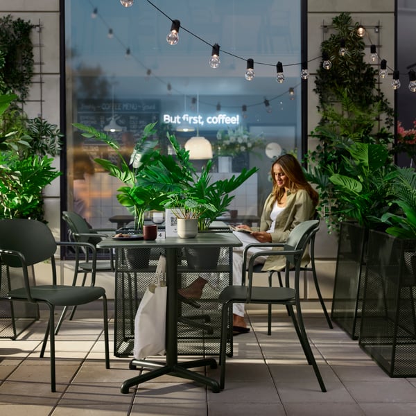Café-Außenbereich mit tiefgrünen VISINGSÖ-Tischen, Metallstühlen und einer lesenden Person.
