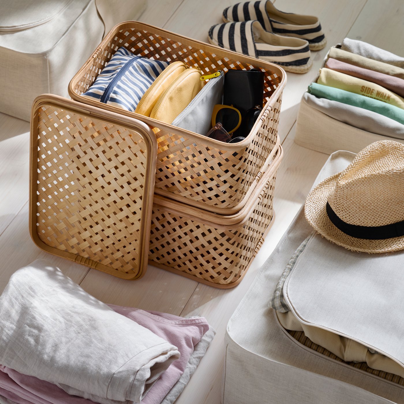 A close-up of 2 stacked VIELÅNGEN boxes with a lid surrounded by summer clothes being packed away in PURRPINGLA storage cases.