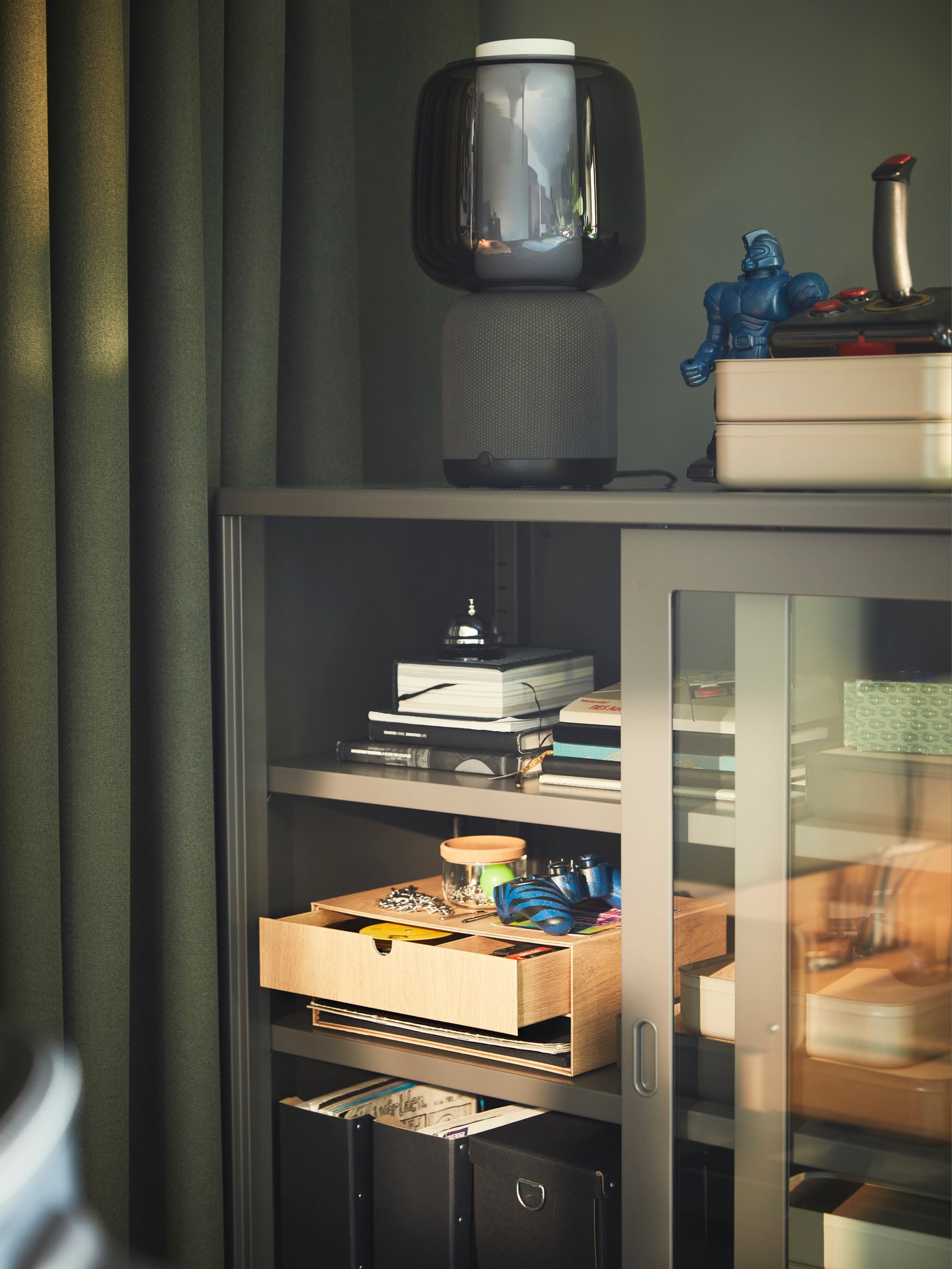 A green-coloured room with an IDÅSEN glass-door cabinet with accessories and a HÄSTVISKARE mini chest of drawers inside.