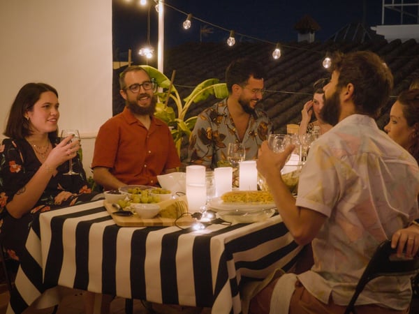 Group of friends on a balcony gathered around a table with food and drinks served.