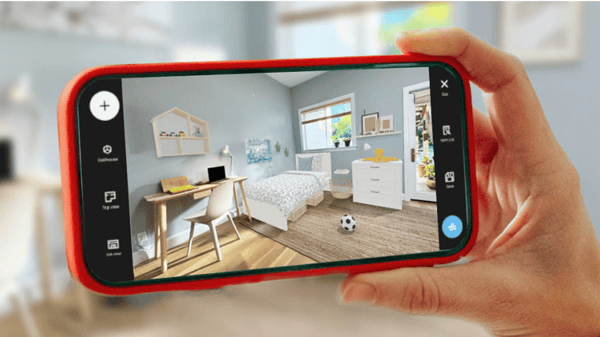 Primo piano di una persona che tiene in mano uno smartphone inclinato, sul cui schermo è visibile la funzione iKREATIV dell'app IKEA con un soggiorno arredato. 