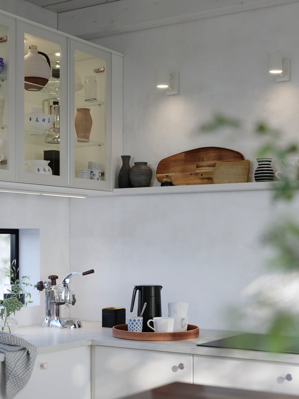 A light kitchen with glossy white RINGHULT fronts, wall cabinets with HEJSTA glass doors and a white wall shelf.