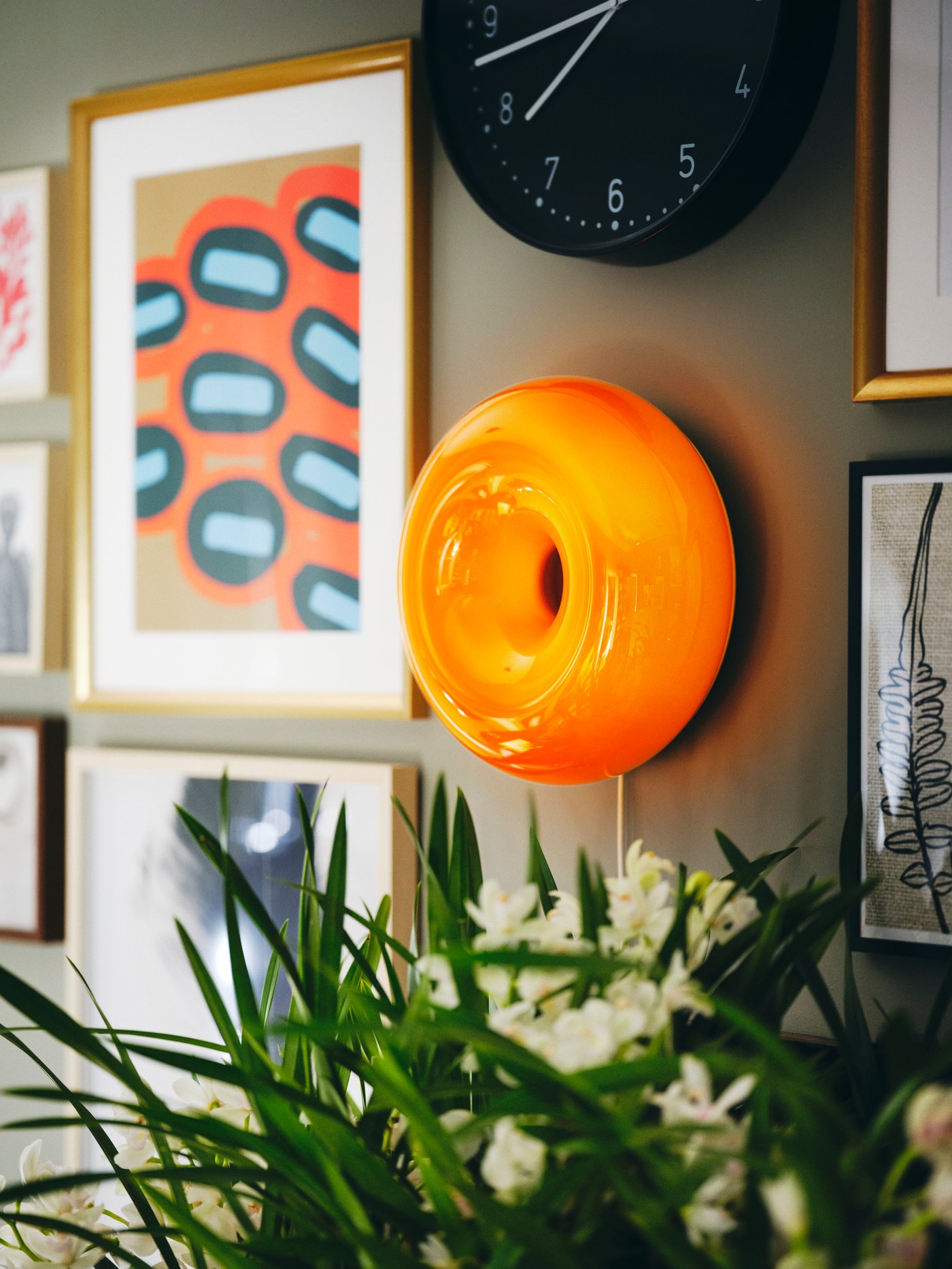 Een oranje VARMBLIXT donut led-lamp en een zwarte BONDIS wandklok aan de muur.