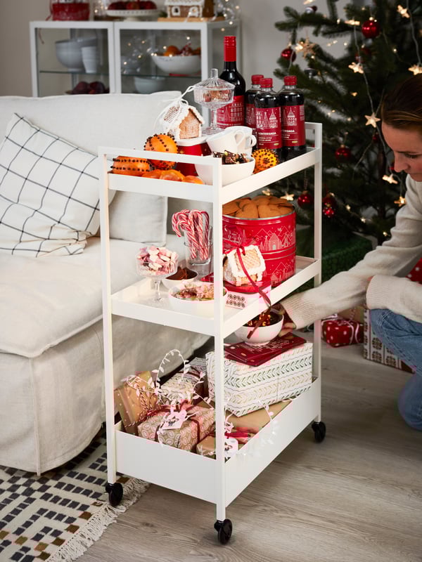 Un carrello bianco con cibi e dolcetti VINTERSAGA. Dietro, un albero di Natale e una persona mentre sta sistemando i prodotti.