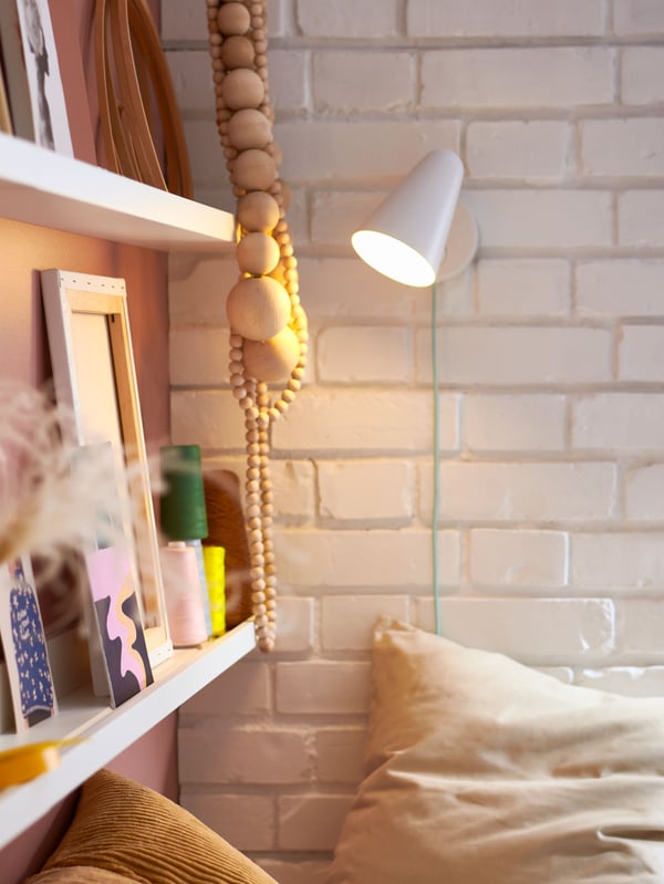 Al costado de una cama hay dos repisas MOSSLANDA blancas con objetos como cuadros y decoraciones.