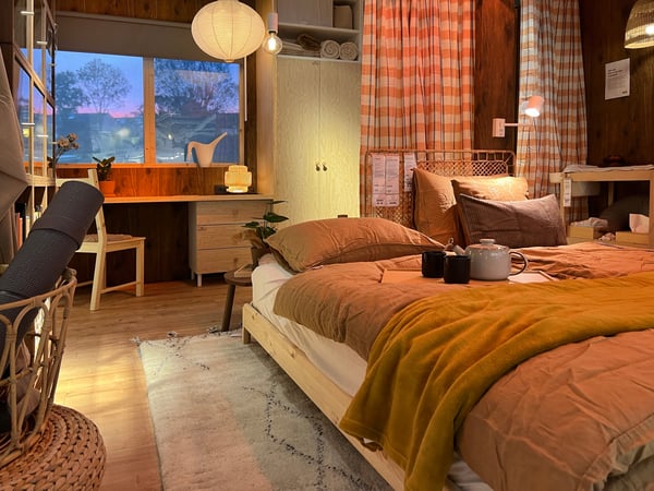 A bedroom with a natural look with a wooden floor, wooden bed, checkered curtains and a wooden chair with desk.