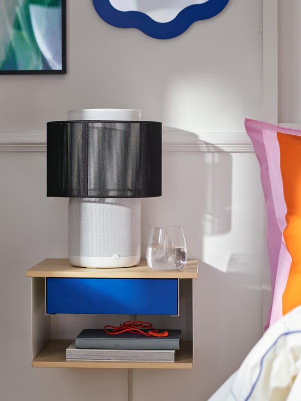 Close-up of wall-mounted bedside table with black and white SYMFONISK speaker lamp with wi-fi on top of it.