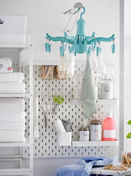 A SKÅDIS white pegboard combination with hooks and shelves holding clothes pegs, cleaning supplies and smaller laundry items.