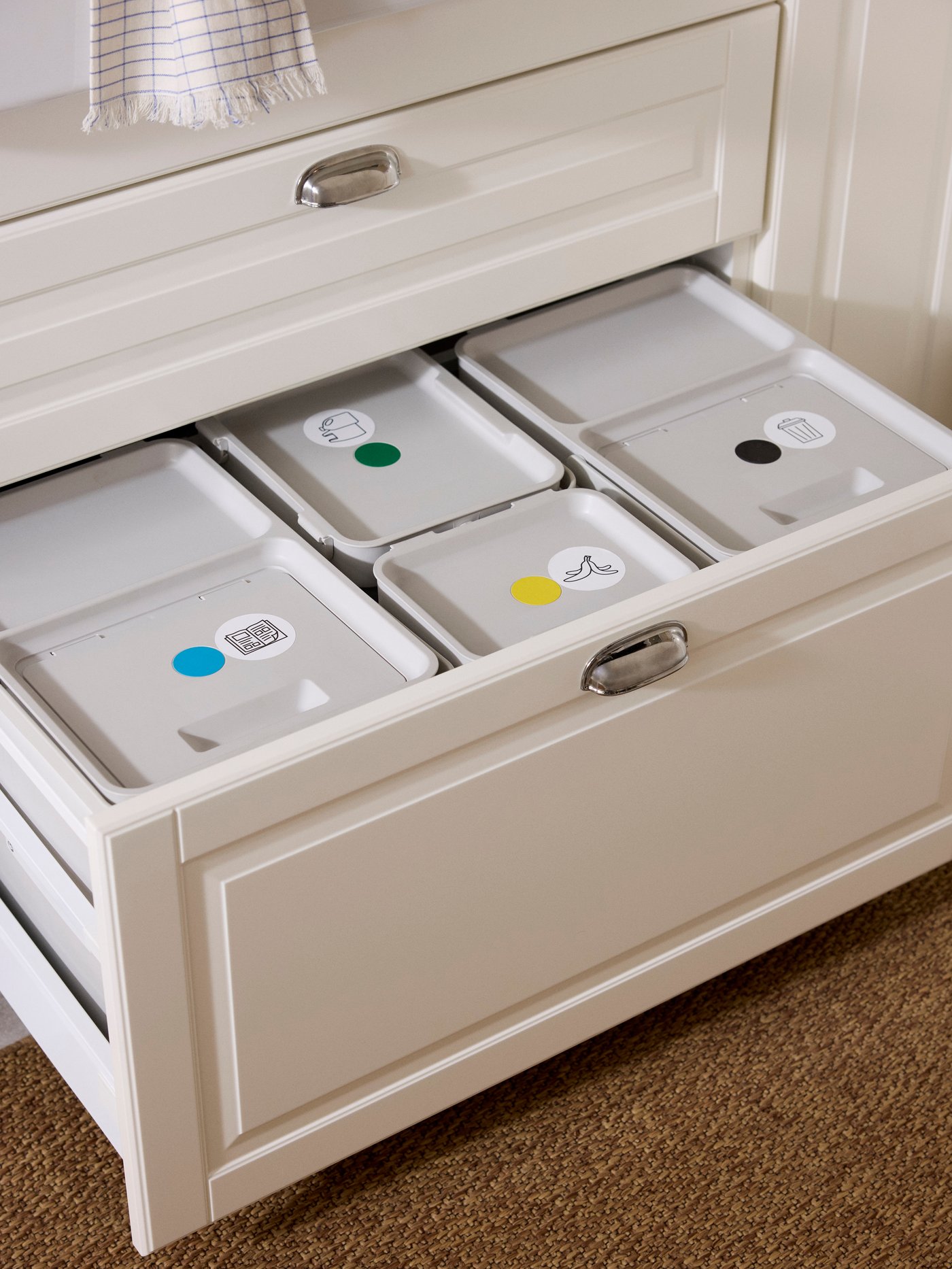 A deep kitchen drawer under a sink open to show recycling bins organised inside with colour dots and symbols.