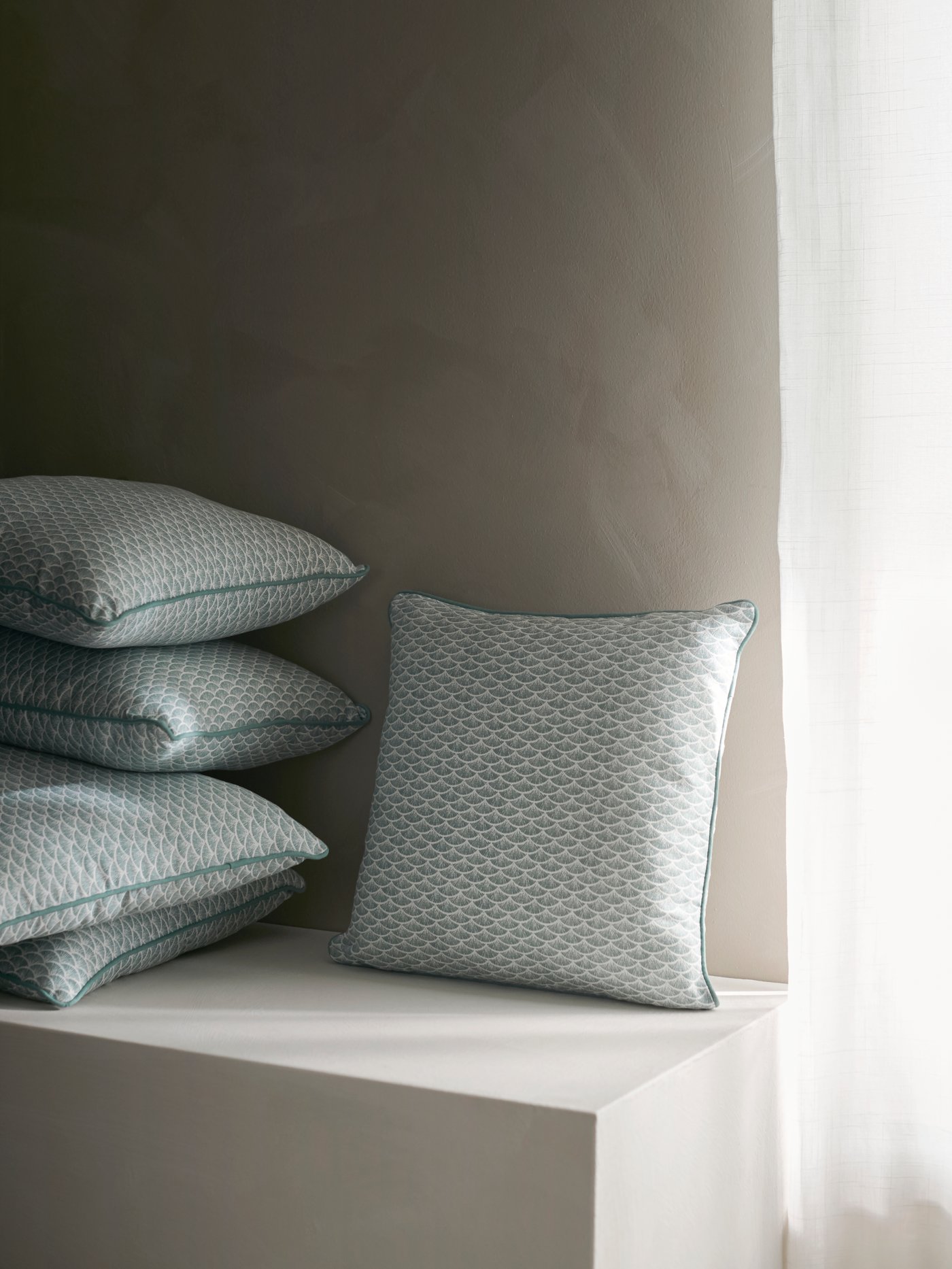 A generous pile of KASKADGRAN cushions are placed on a built-in ledge, illuminated by soft light from the nearby window.