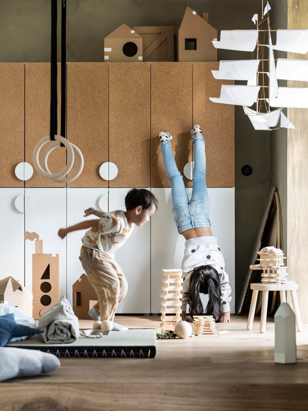 twee kinderen zijn aan het spelen. Een kind beoefent gymnastiek en staat op de handen met de voeten tegen de muur.
