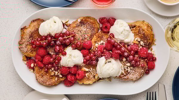 A white oval dish has several pieces of French toast with ice-cream, fresh raspberries, red currants and almonds on it.