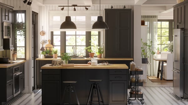 A big kitchen with black-stained LERHYTTAN fronts and a wooden countertop has a kitchen island and two black pendant lamps.