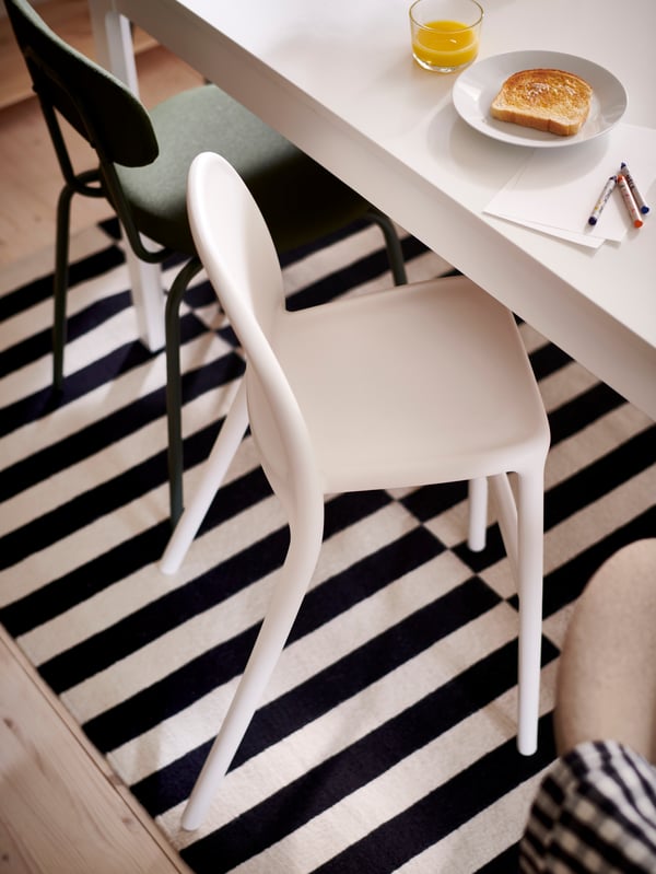 A white URBAN junior chair and a deep green ÖSTANÖ chair stand at an EKEDALEN extendable table on a striped STOCKHOLM rug.