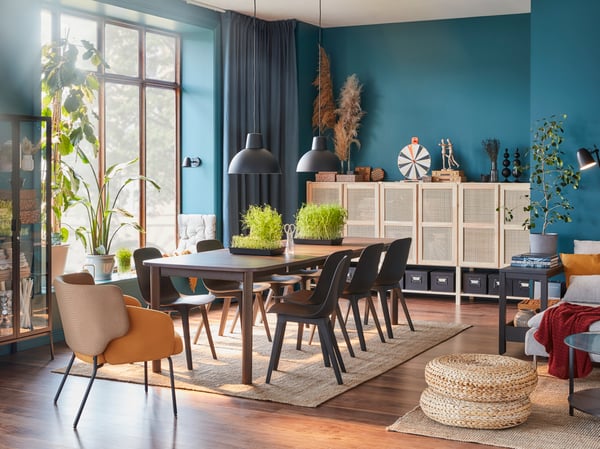 A large dark brown table, eight anthracite chairs, a yellow armchair and a storage system with bamboo doors.