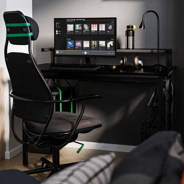 LÖPARBANA gaming-aulki beltza UTVISNING gaming-idazmahai beltzaren ondoan. NÄVLINGE laneko lanpara beltz bat dago idazmahaian.