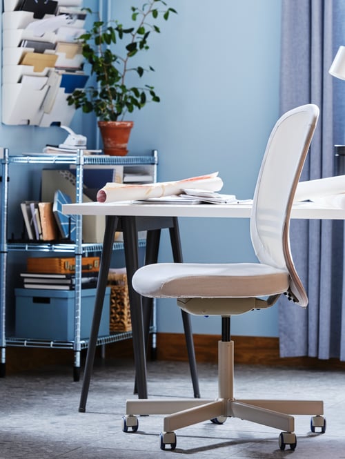 Arbeitsplatz mit Schreibtisch, Drehstuhl mit Rollen, Regal, einer Pflanze in einem Übertopf, Aufbewahrungsboxen, Schreibutensilien und Papier.
