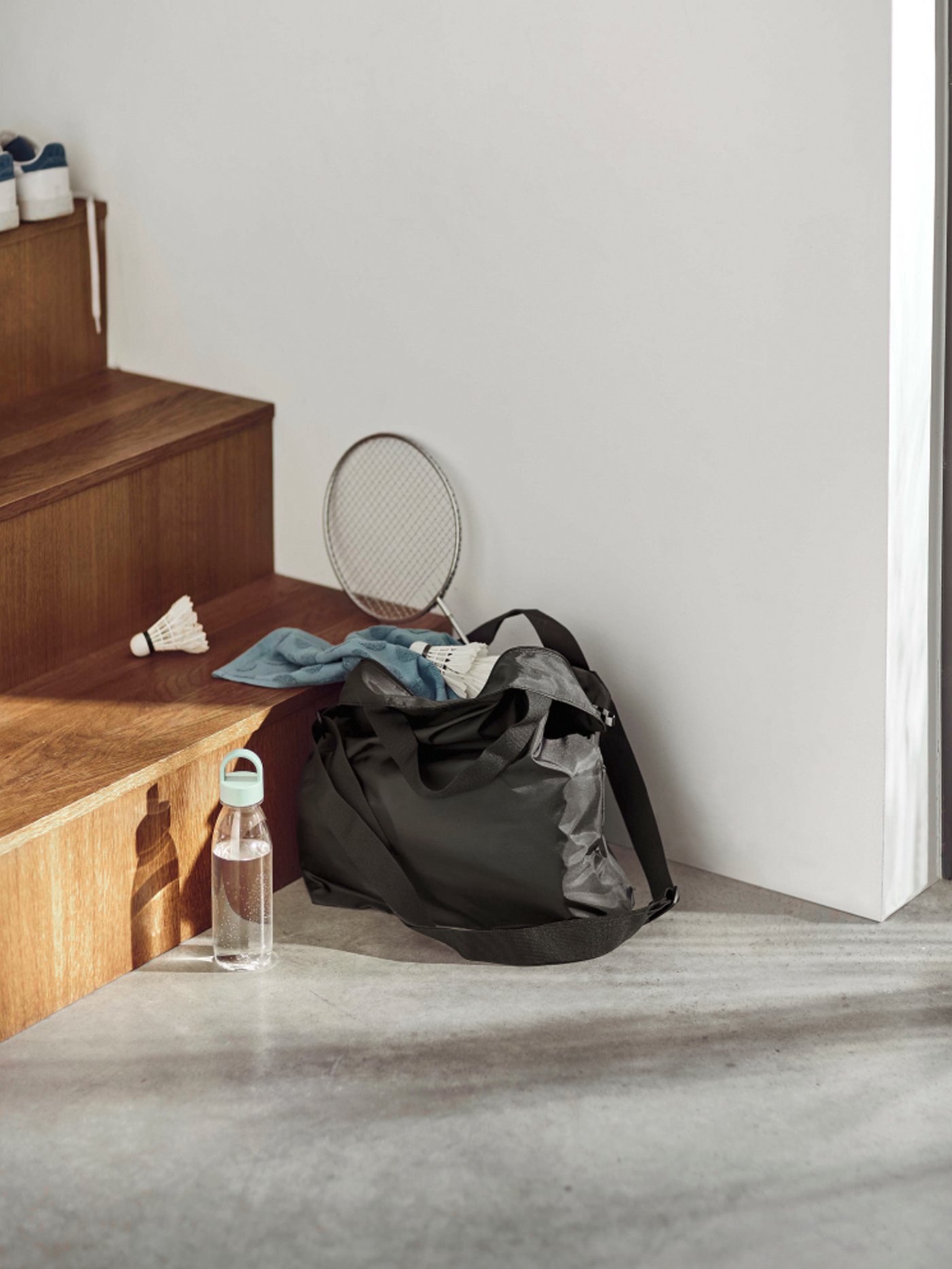 Le sac RÄCKLA est posé au bas d’un escalier, bien rempli avec tout l’équipement pour une partie de badminton.