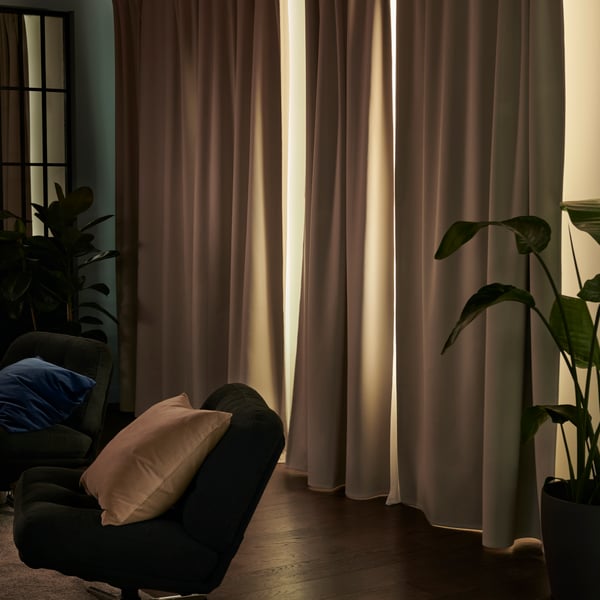 Beige KORGMOTT block-out curtains elegantly drape in a cosy living room, partially opened to reveal soft, natural light.