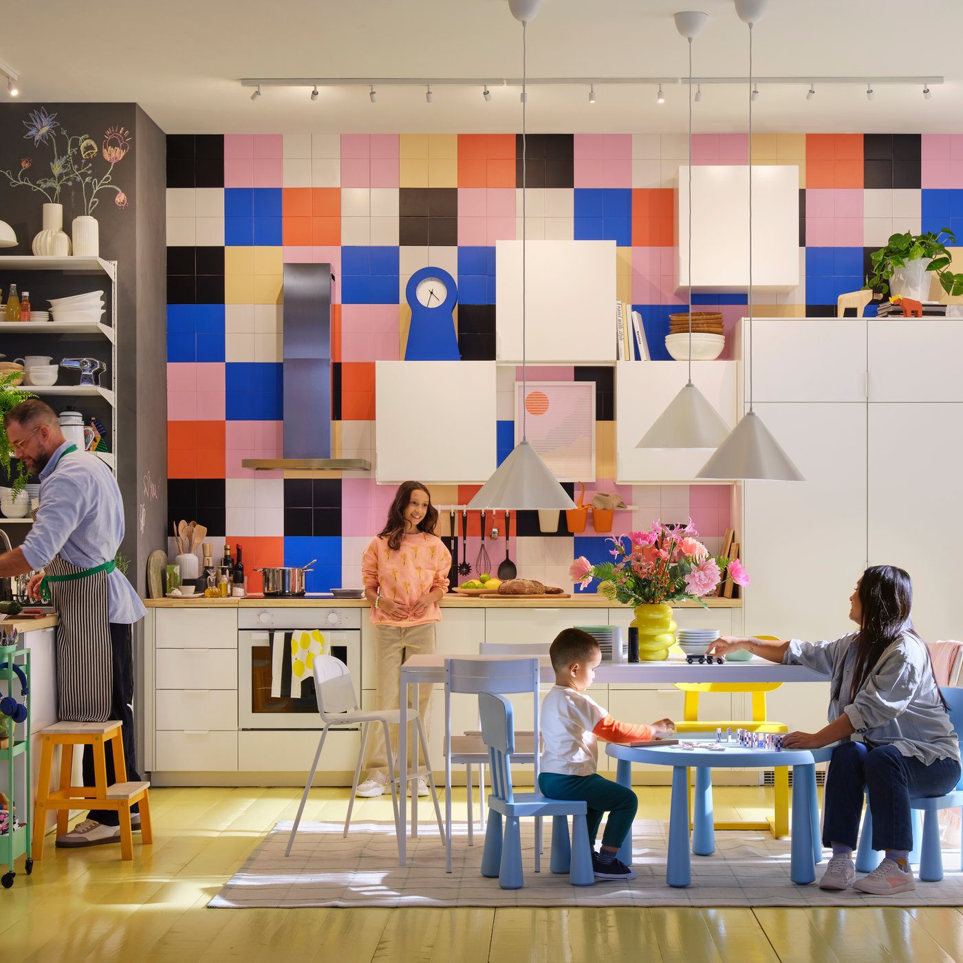 A family of five spends time together in a white modern kitchen with large, brightly coloured tiles and a high ceiling.