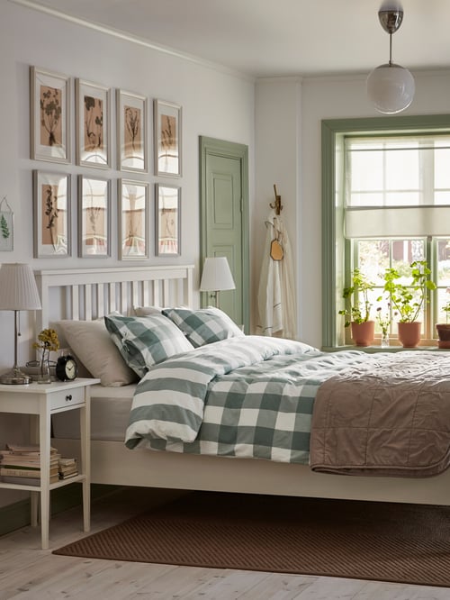 A bright bedroom with a white-stained, solid pine HEMNES bed frame and a green/white quilt cover by bedside tables.