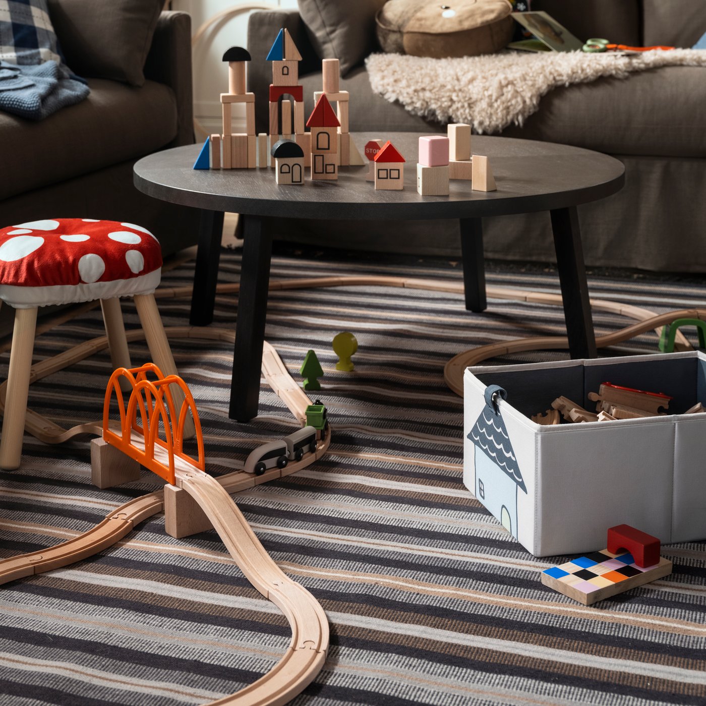 Giochi della serie LILLABO, uno sgabello e un contenitore BARNDRÖM sono posti su un tappeto a tessitura piatta RÅVAROR in una sala da pranzo.
