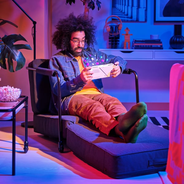 A person sitting in a BRÄNNBOLL gaming lounge chair using a tablet that has coloured pixel graphics coming from the screen.
