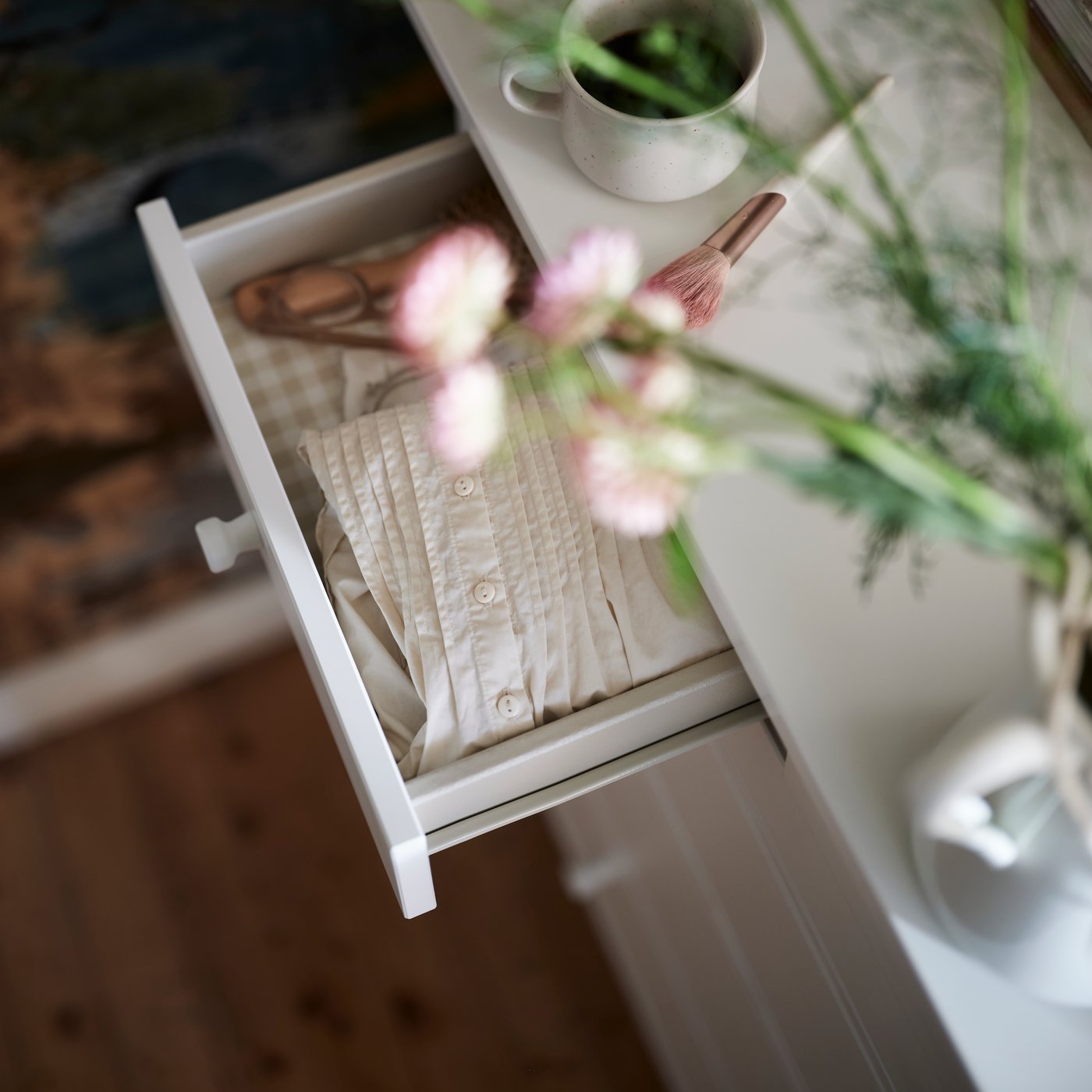 En GULLABERG-kommode med 6 skuffer i hvitt med én skuff trukket ut, vist med en plante over i et rustikt rom.