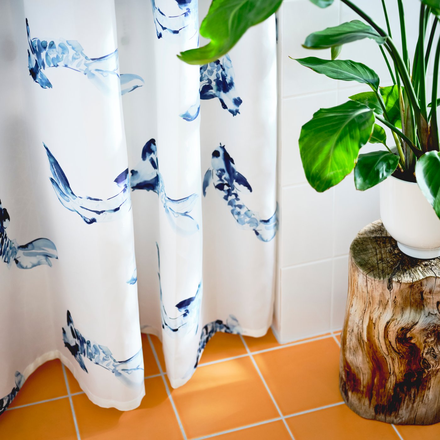 Kylpyhuoneessa on valkoinen, sinikuvioinen VATTENSJÖN-suihkuverho ja suuri huonekasvi.