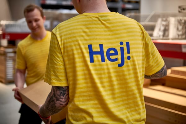 Two IKEA co-workers lifting a package at warehouse.